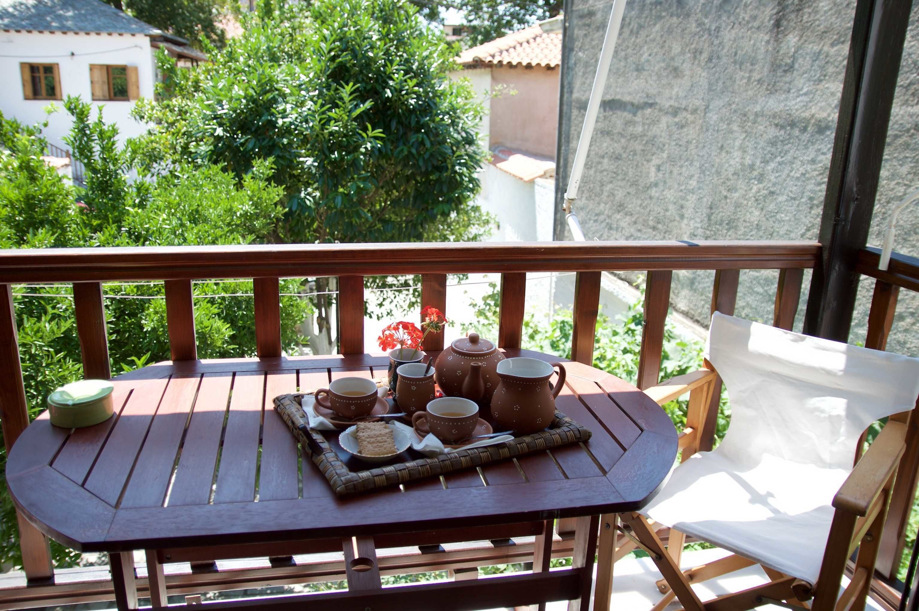Une table en bois sur laquelle est posé un plateau avec un service à thé, le tout sur un balcon.