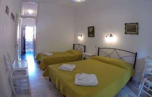 Habitación de hotel con dos camas, una mesita de noche pequeña, una silla y una puerta que da a un pasillo.