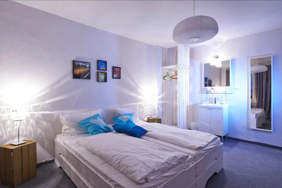 A bedroom with a large bed, white walls, and a small bedside table.