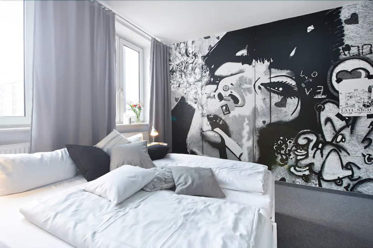 A bedroom with a bed, pillows, a window, and a wall with graffiti art.