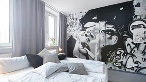 Un dormitorio con cama, almohadas, una ventana y una pared con arte callejero.