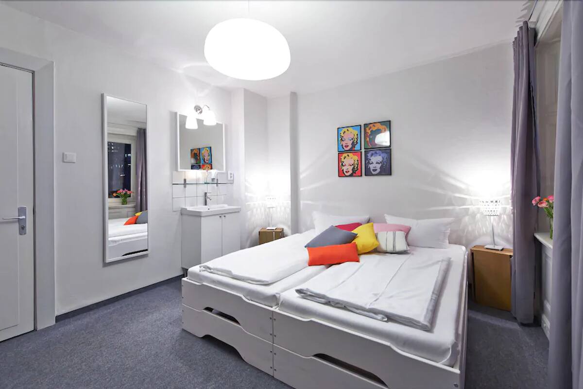 A modern bedroom with a bed, bedside tables, a mirror, and artwork on the wall.