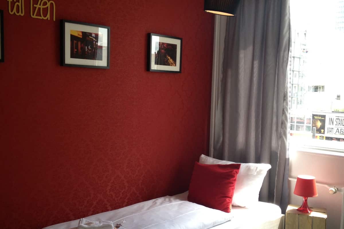 A bedroom with a white bed, red pillows, and two framed pictures on the wall.