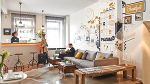 Un moderno vestíbulo de hotel con mostrador de recepción, área de bar y zona de estar con sofá y mesa de centro.