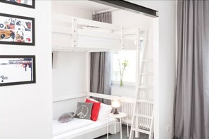 Una cama litera con estructura blanca, una mesita de noche con lámpara, y una ventana con cortinas.