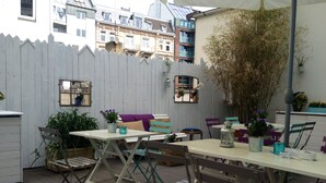 Un patio exterior con mesas y sillas, rodeado por una valla de piquetes blanca y plantas en macetas.