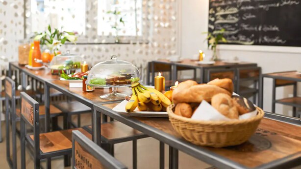 Un ambiente de restaurante con una larga mesa mostrando alimentos como plátanos, pan y una cesta de pasteles.
