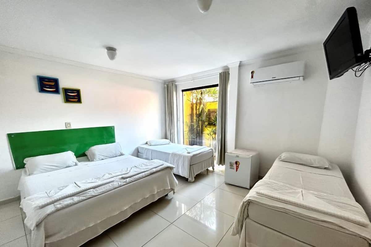 A hotel room with two single beds, a large bed, a flat-screen TV, and a small refrigerator.