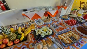 Una mesa de buffet con diversos alimentos, entre ellos frutas, pasteles y pan.