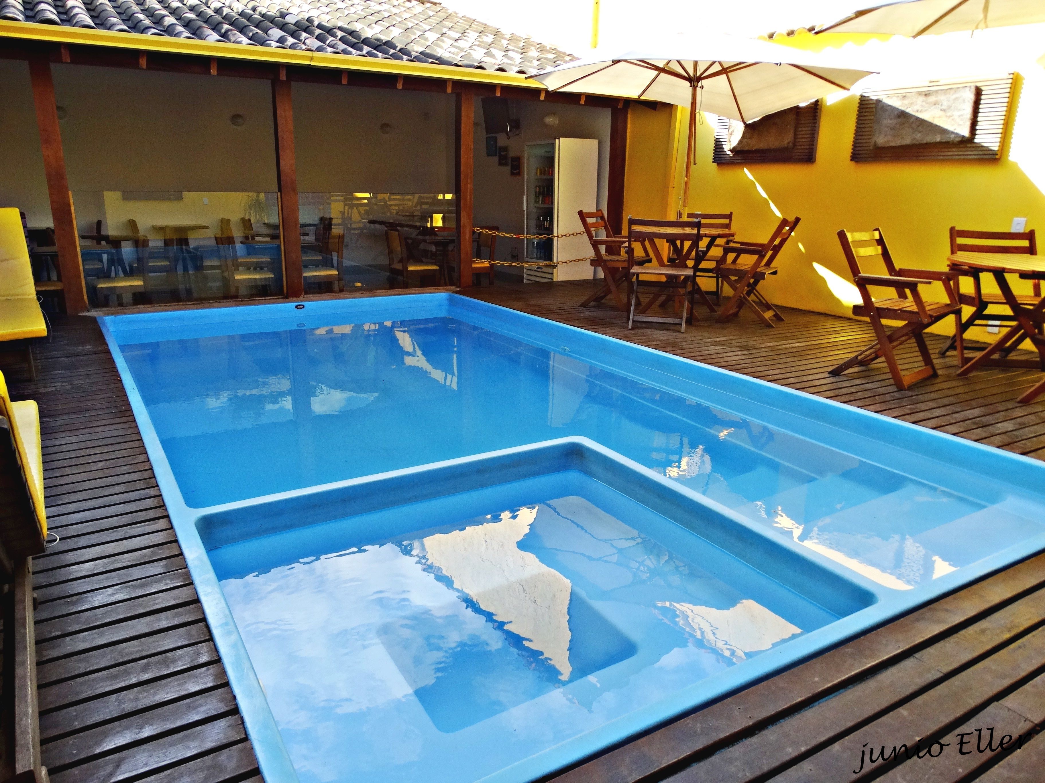 Una piscina con cubierta de madera, rodeada de mobiliario exterior y una pared amarilla.