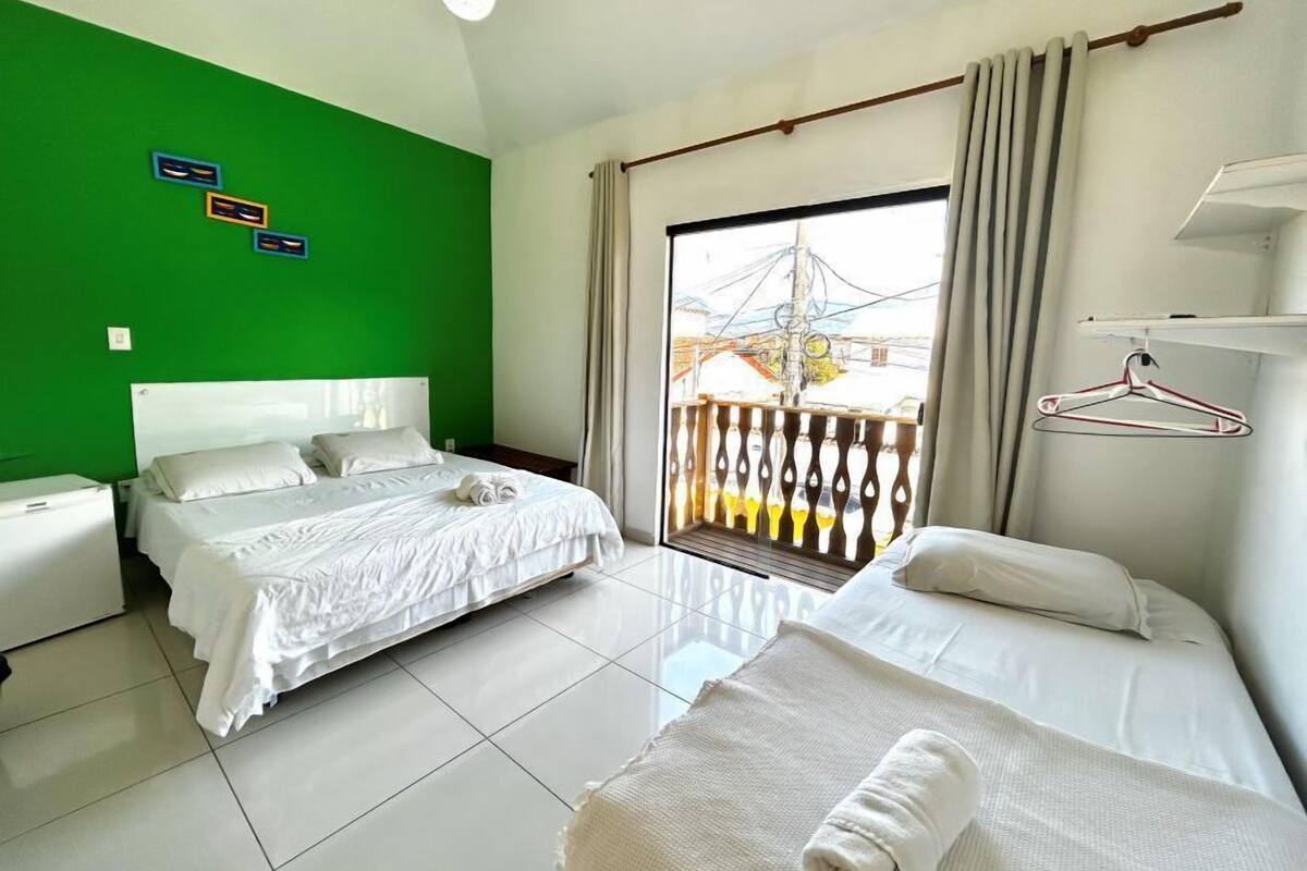 A hotel room with two beds, a green wall, a balcony with a view, and a hanging clothes rack.