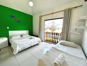 A hotel room with two beds, a green wall, a balcony with a view, and a hanging clothes rack.