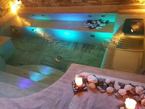 A hot tub with a stone floor, a stone wall, and a candle on a table. - Aurelia Garden Gold Bed & Breakfast (Rome)