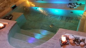 Espaço de spa com paredes de pedra, hidromassagem, uma pequena piscina e área de estar com velas.