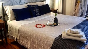 Cama arrumada com decoração em formato de coração, uma garrafa de vinho e um tabuleiro com petiscos.