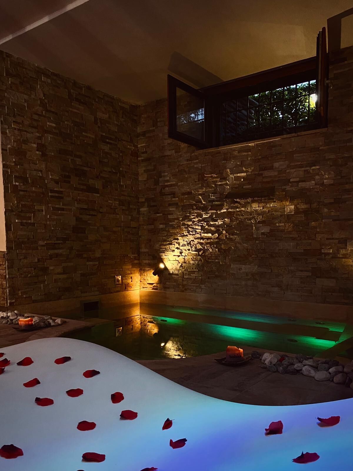 A spa area with a stone wall, a small pool, and rose petals on the floor.
