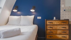 A bedroom with a bed, a wooden dresser, and two wall-mounted lights.