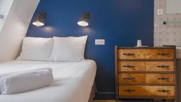 Une chambre à coucher avec un lit, une commode en bois et deux lampes fixées au mur.
