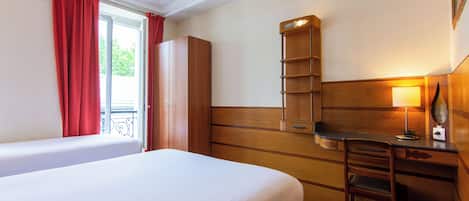 Ein Hotelzimmer mit einem Bett, einem Schreibtisch mit Lampe, einem Kleiderschrank und einem Fenster mit Vorhängen.