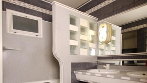 A modern bathroom with a bathtub, two sinks, a large mirror, and a decorative clock. - Hôtel Marignan (Paris)