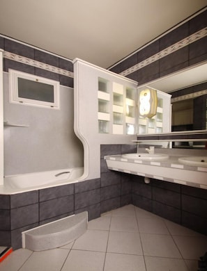 Un baño moderno con bañera, dos lavabos, un espejo grande y un reloj decorativo.