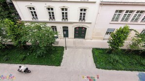 A building with a symmetrical facade, a central entrance with double doors, and a paved area with a hopscotch game. - Hôtel Marignan (Paris)