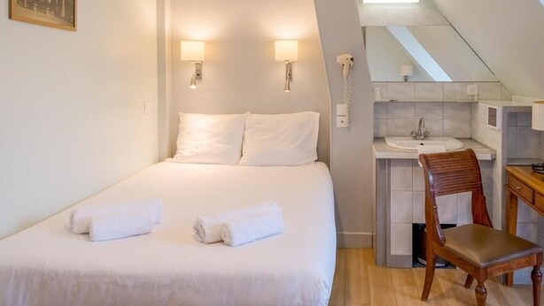 A bedroom with a bed, two wall-mounted lamps, a telephone, and a small bathroom with a sink and mirror. - Hôtel Marignan (Paris)