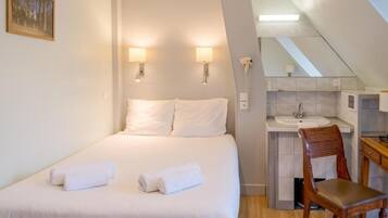 A bedroom with a bed, two wall-mounted lamps, a telephone, and a small bathroom with a sink and mirror.