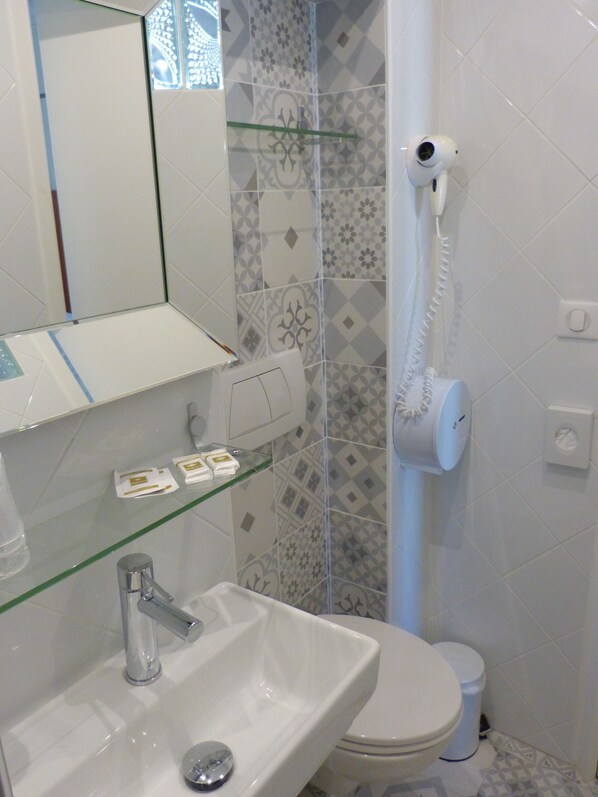 Un baño con un lavamanos blanco, un espejo, un estante de vidrio con artículos de aseo, un inodoro y un secador de pelo montado en la pared.