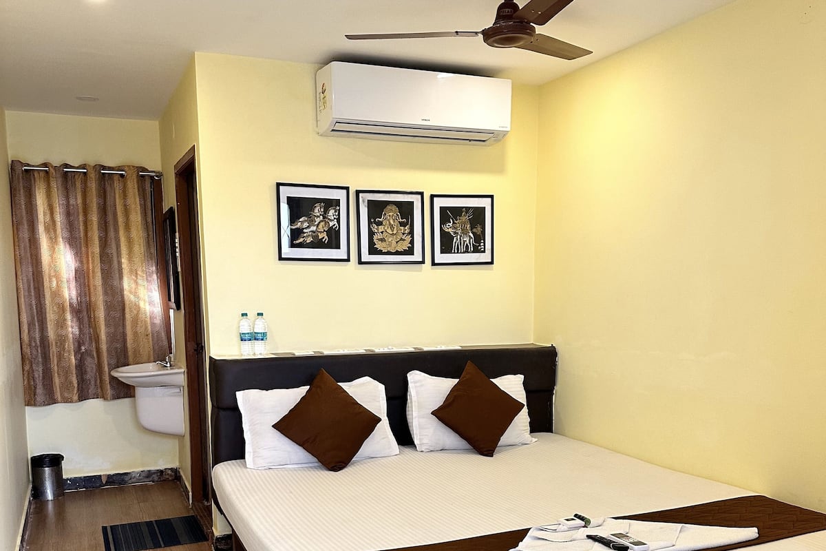 A hotel room with a large bed, a ceiling fan, an air conditioning unit, a shower curtain, and three framed pictures on the wall.