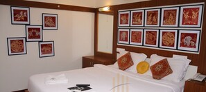 A hotel room with a large bed, multiple framed pictures on the walls, a wooden headboard, and a bedside table with a phone. - Hotel Ramakrishna (Tirukalukundram)