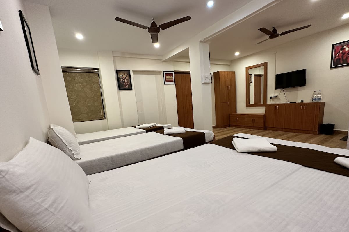 A hotel room with two single beds, a wooden wardrobe, a television, and ceiling fans.