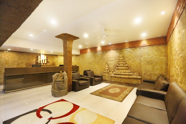 A hotel reception area with a reception desk, seating area, and a decorative wall with a textured pattern. - Hotel Ramakrishna (Tirukalukundram)