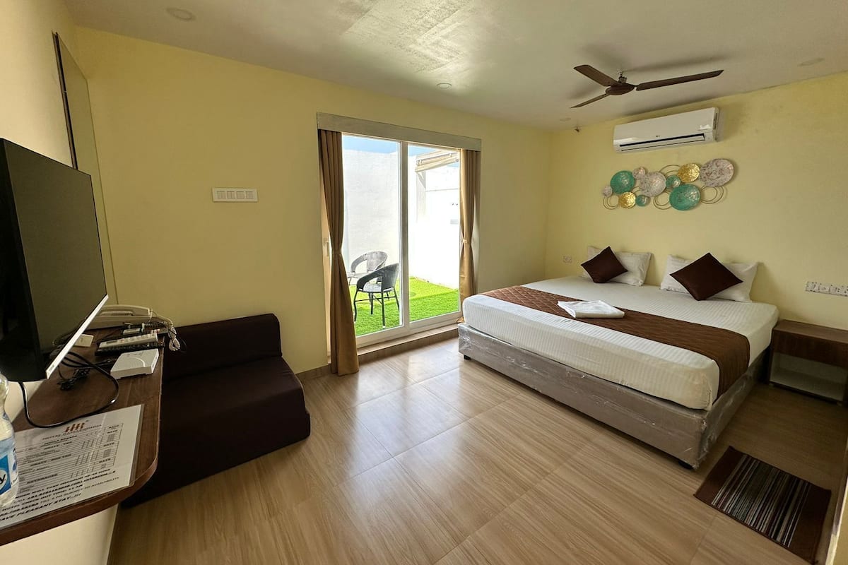 A hotel room with a bed, a desk with a computer, a TV, and a sliding glass door to a balcony.