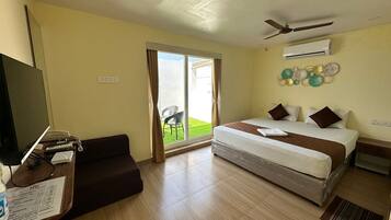 Habitación de hotel con cama, escritorio con computadora, televisor y puerta corrediza de vidrio a un balcón.