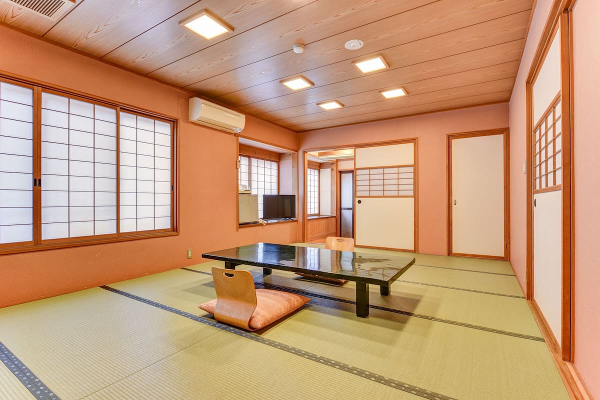 Una habitación con esteras de tatami, una mesa baja, cojines, puertas correderas y un televisor.