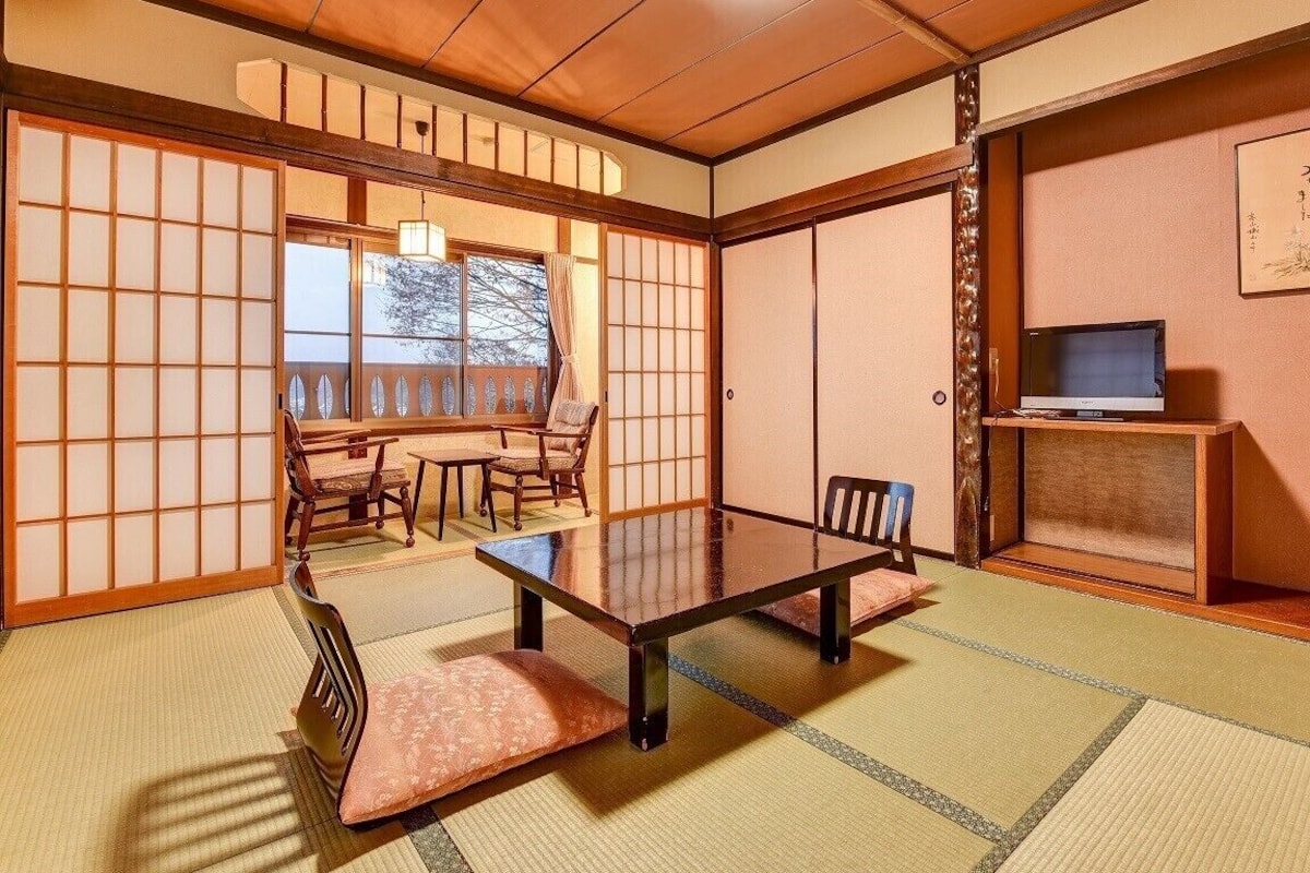 Una habitación japonesa tradicional con suelo de tatami, una mesa baja y puertas correderas.