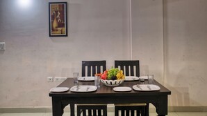 Une table à manger dressée avec des assiettes, des couverts et un panier de fruits.