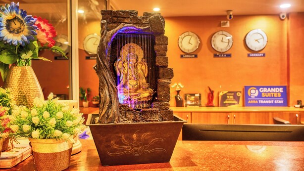 Une statue illuminée d’une lumière bleue, placée dans une structure en pierre, entourée de fleurs et d’un panneau indiquant « Grande Suites ».
