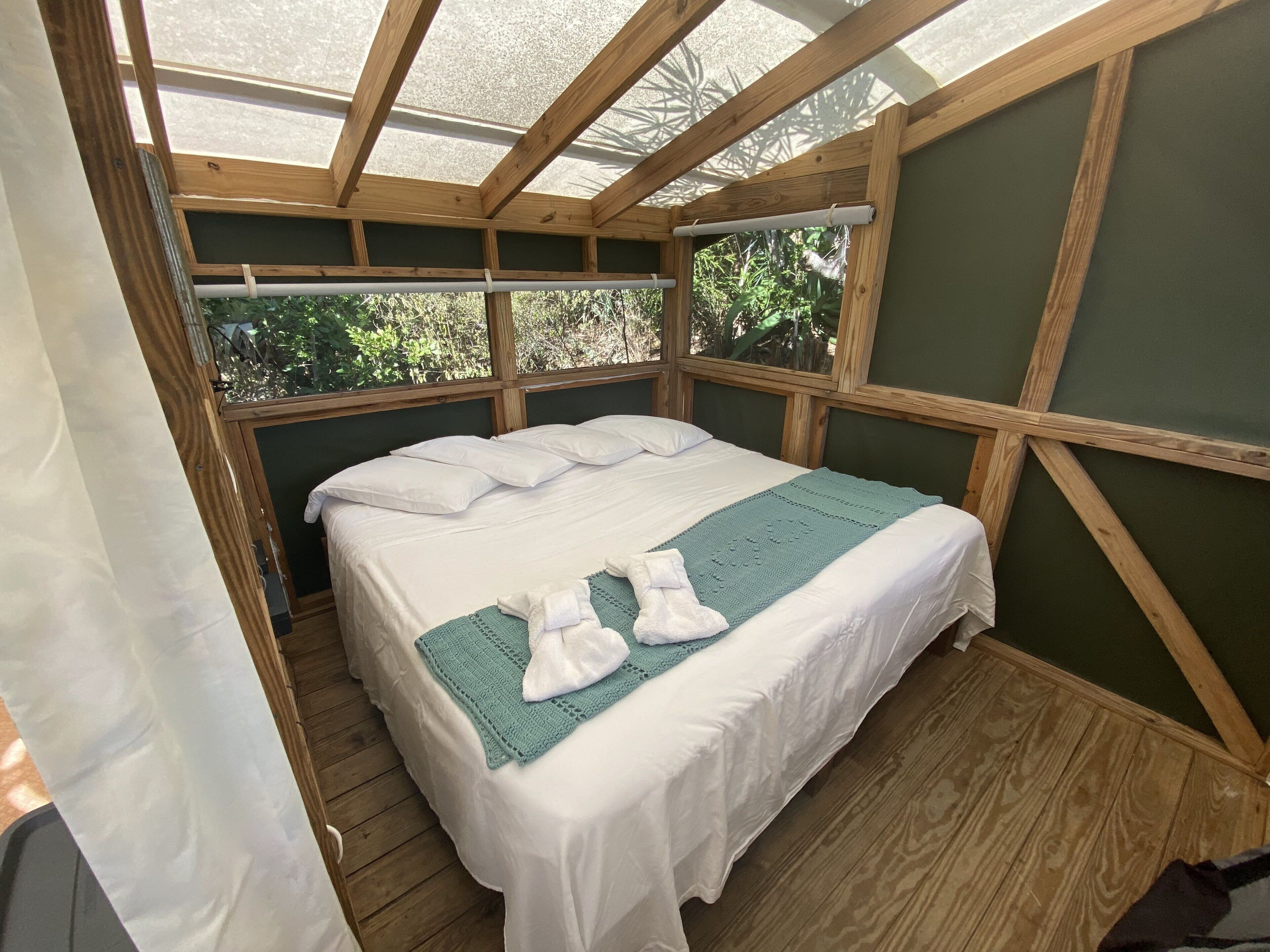 Ein Einzelbett mit weißer Bettwäsche, einer türkisblauen Decke und zwei auf dem Bett gefalteten Handtüchern. Der Raum hat Holzbalken und eine grüne Wand.