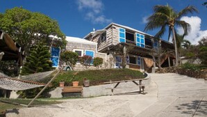 Une propriété située en bord de mer, avec une grande maison dotée d’un balcon, d’un hamac et d’un chemin de pierre menant à l’entrée.