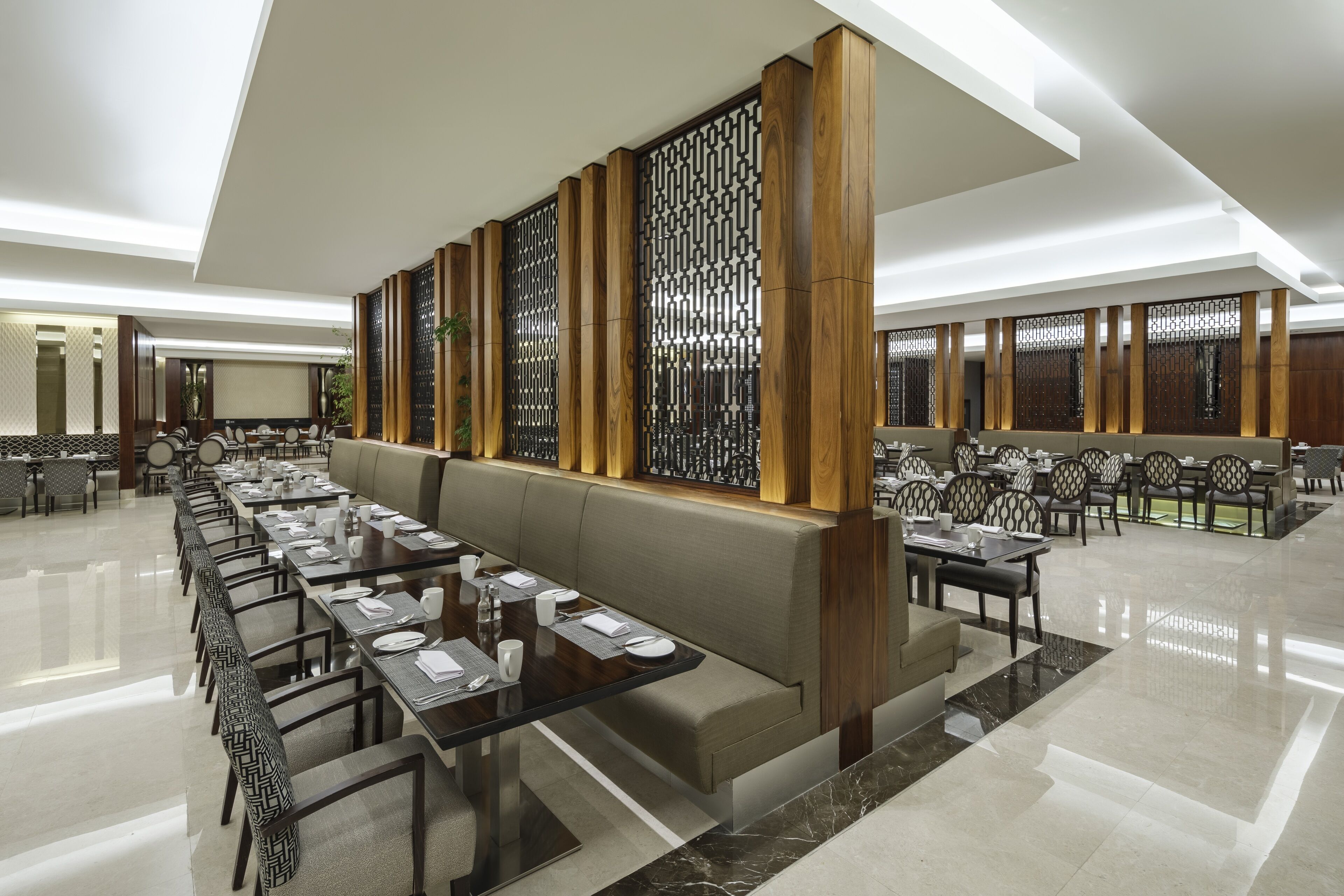 A spacious dining area with long tables and booths, a high ceiling, and a decorative wooden partition.