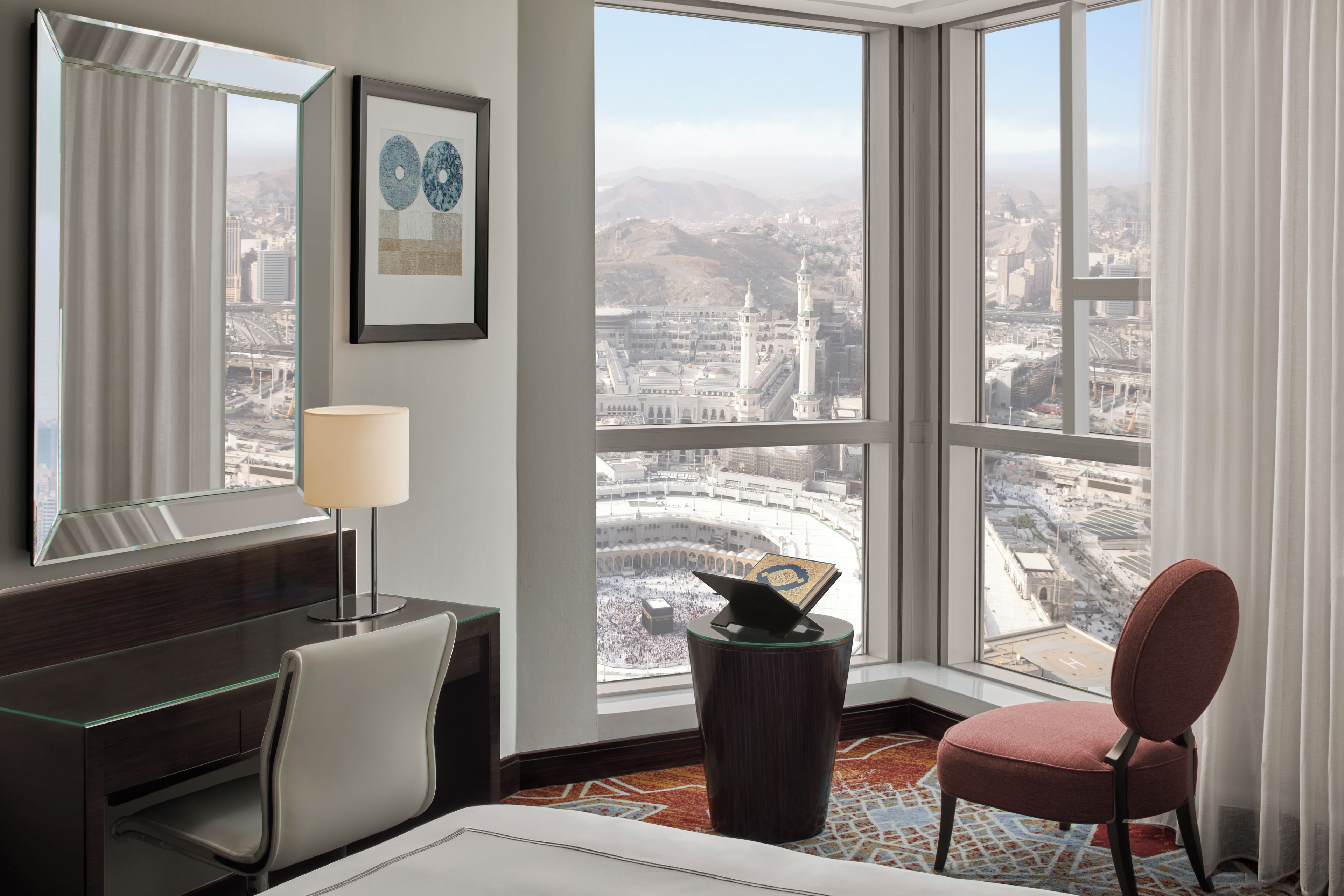 A hotel room with a large window offering a view of a cityscape and a mosque.