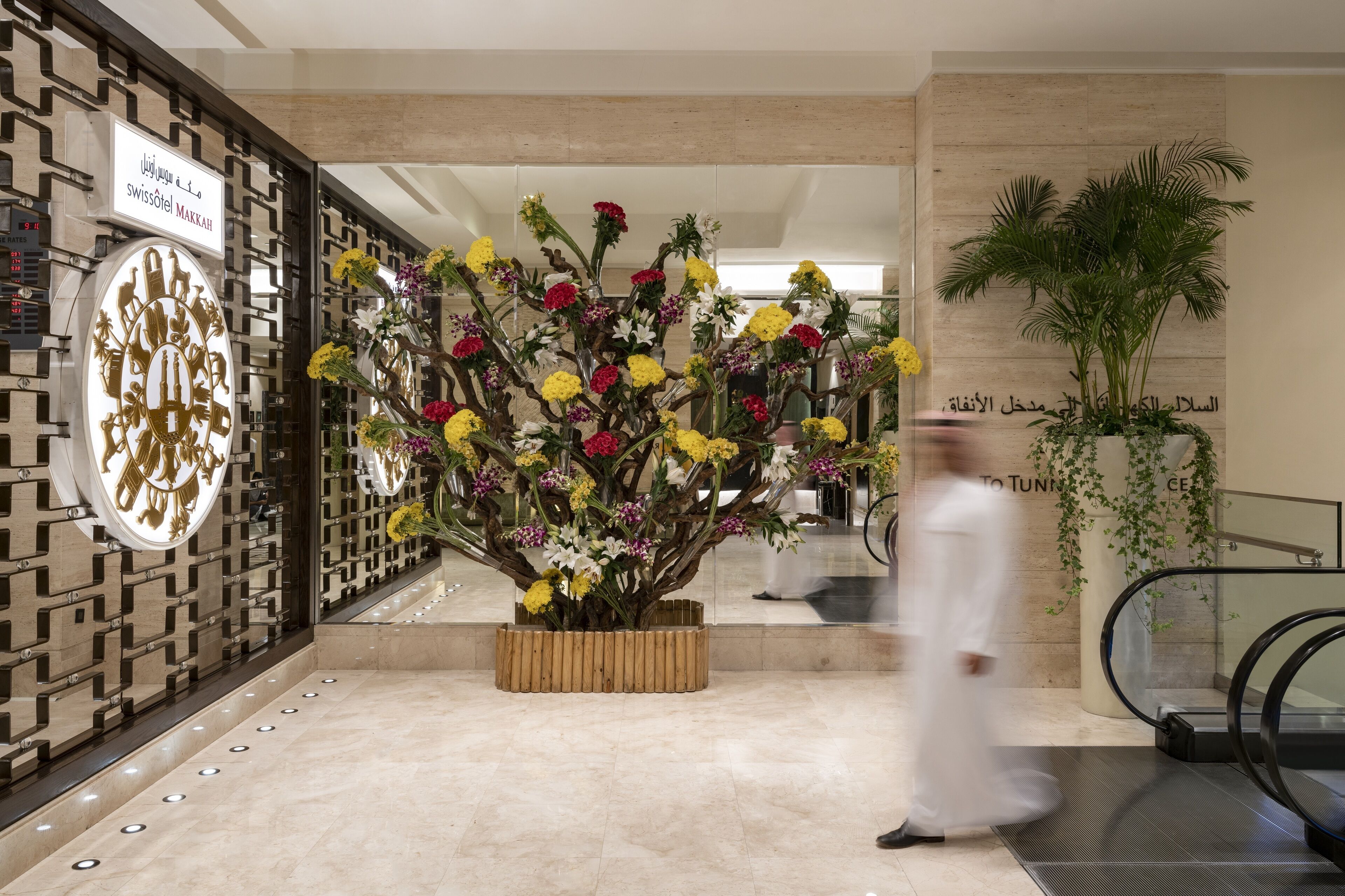 Un vestíbulo con un gran arreglo floral, un letrero de Swissôtel Makkah y un diseño arquitectónico moderno.