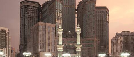 A large mosque with a prominent clock tower and a central courtyard with a black cube structure.