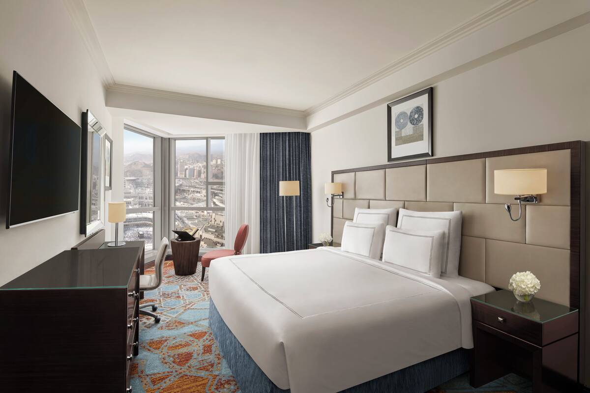 A hotel room with a large bed, a desk, a chair, and a TV.