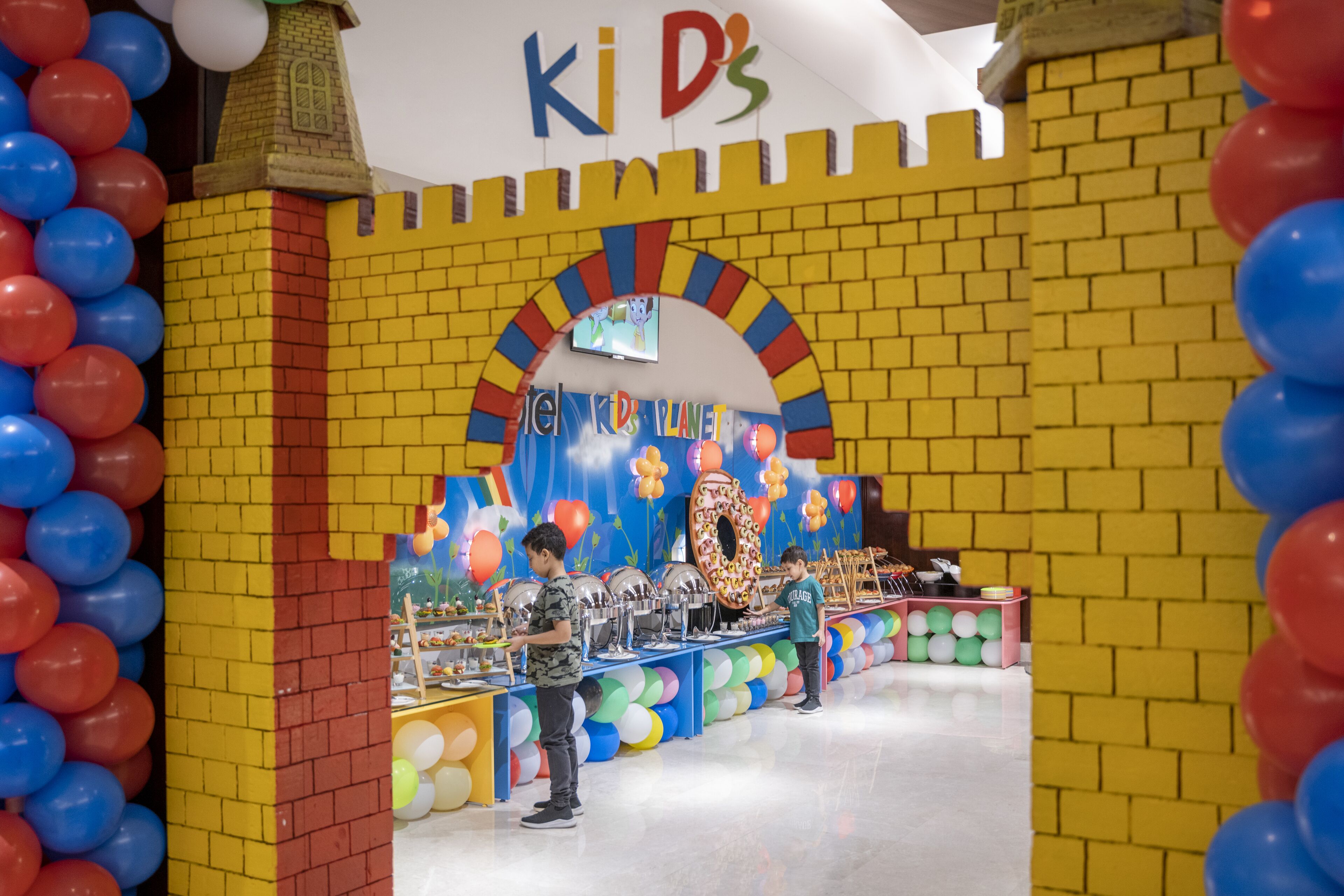 A children's play area with a brick wall, colorful balloons, and a sign that reads "Ki D'S".