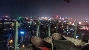 Un balcon doté de meubles en osier et offrant une vue sur la ville la nuit.