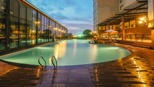 Une piscine dotée d’une enceinte en verre, entourée d’une terrasse en briques et bordée de bâtiments adjacents.