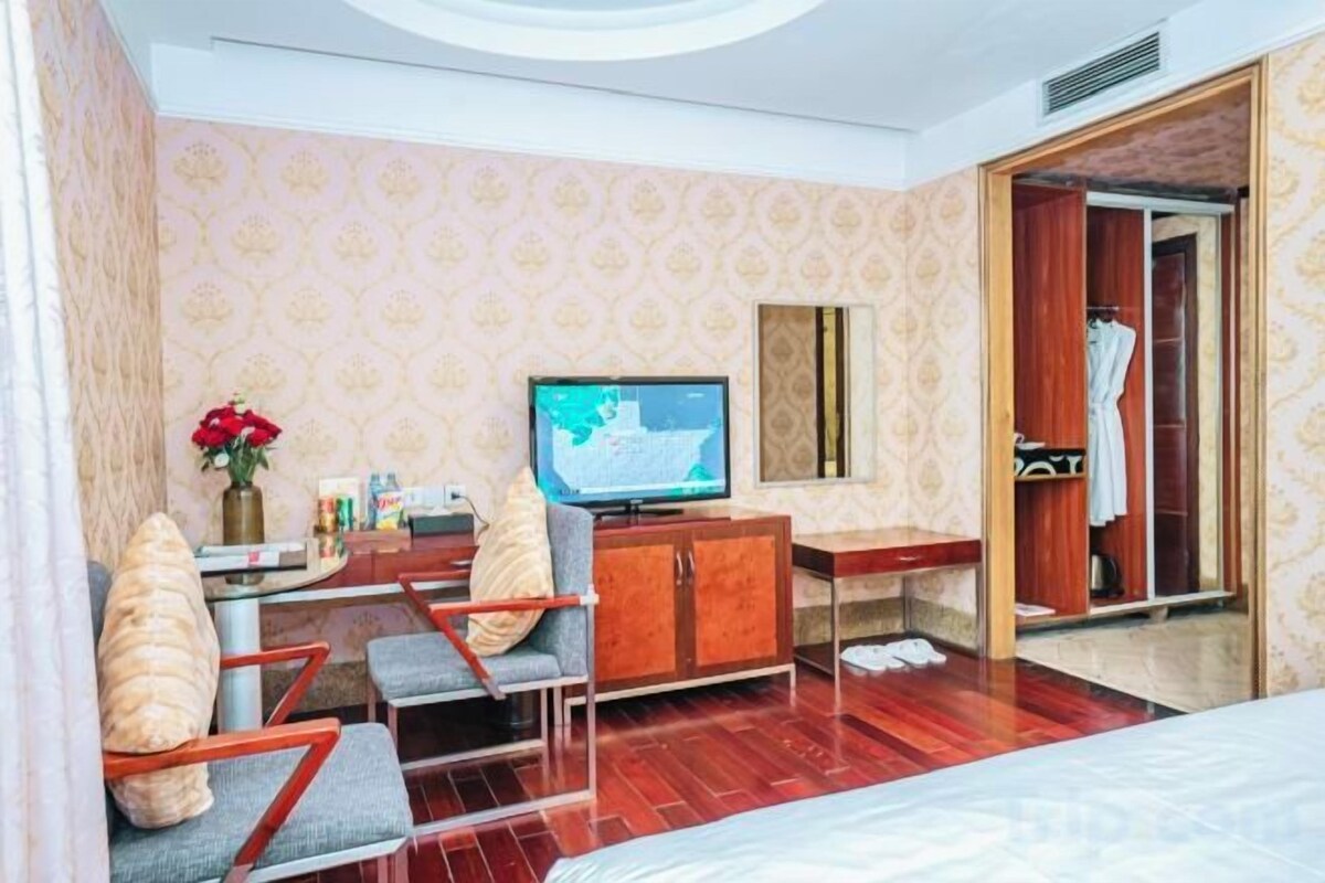 Una habitación de hotel con una cama, televisión, escritorio con computadora, armario y espejo.